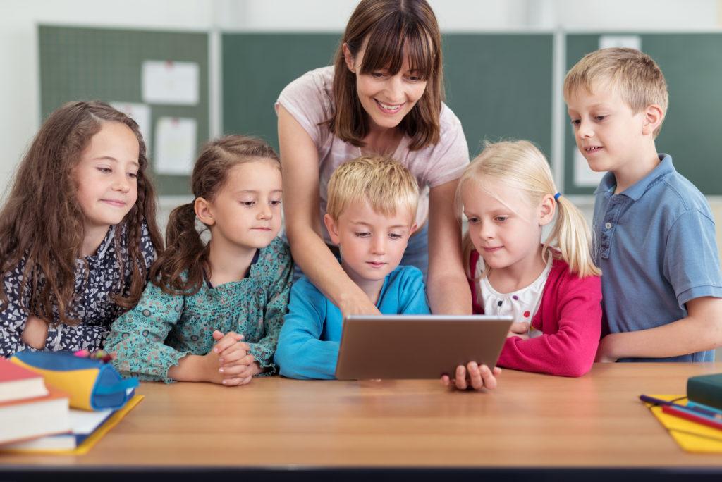 Lehrerin mit Kindern zeigt auf ein Tablet ZDB